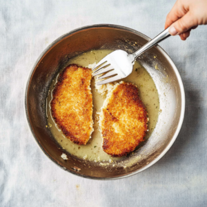 Chicken cutlets frying in a skillet of hot oil, achieving a golden crispy crust.