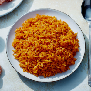 Achiote rice served in a bowl with a bright orange hue, topped with fresh herbs.