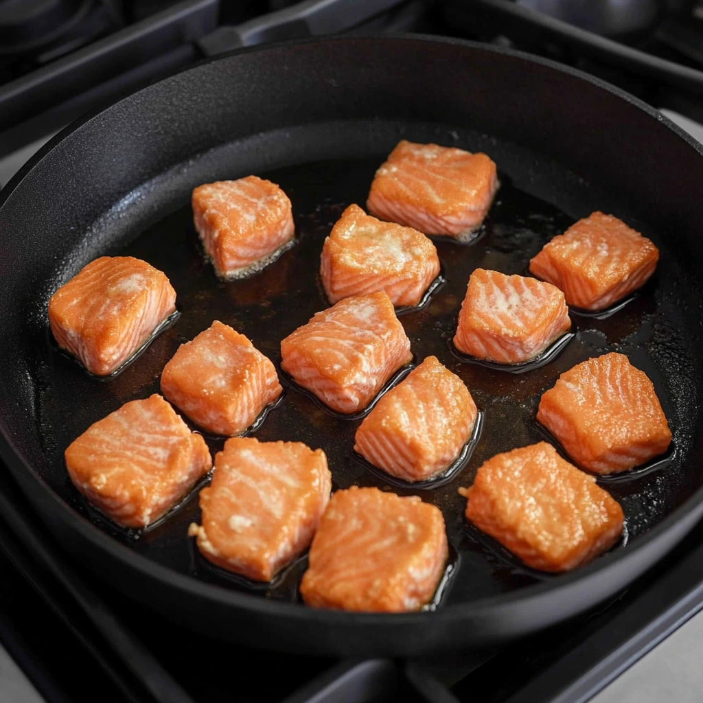 Close-up of fried salmon bites with a side of soy dipping sauce and green onion garnish.