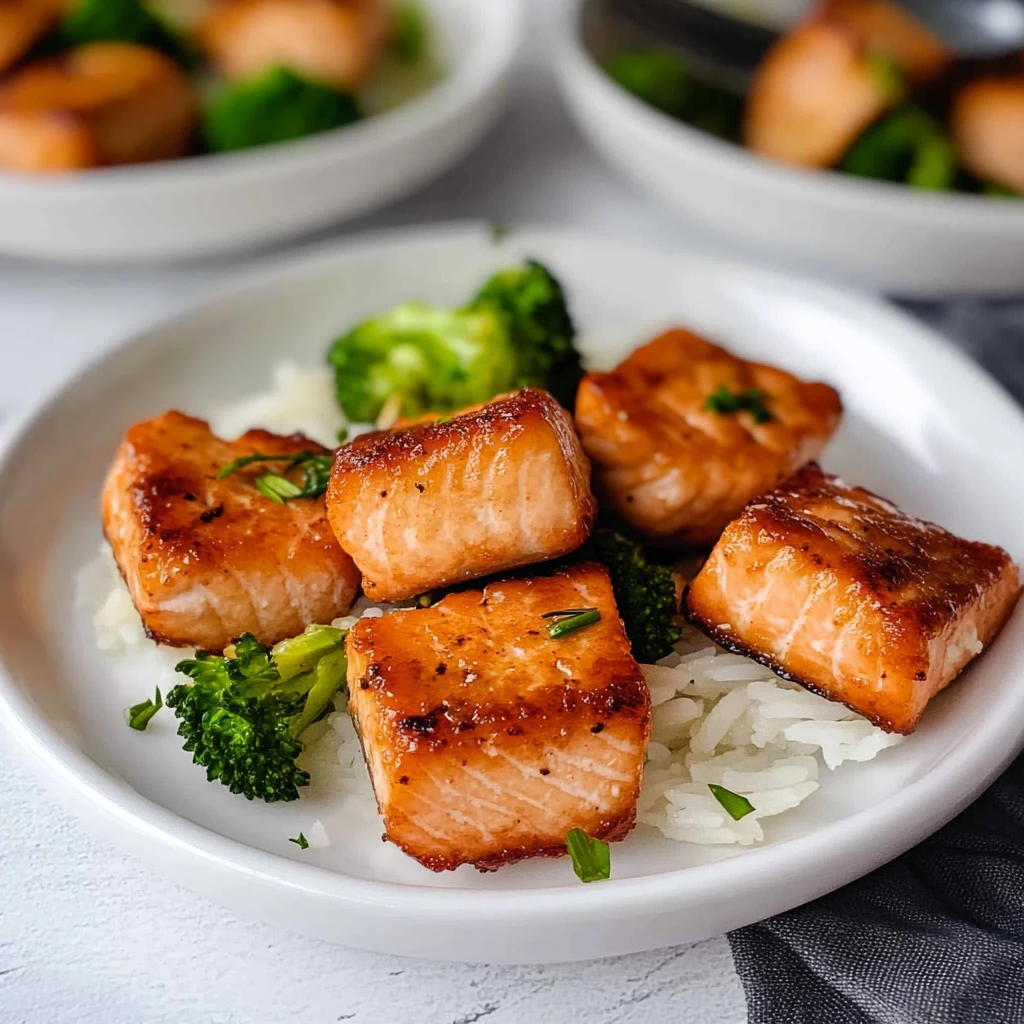 Golden-brown fried salmon bites on a plate, garnished with green onions and served with a soy dipping sauce.